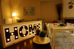Una habitación con un cartel que dice 'HOME', una mesa de comedor, sillas, una lámpara y dos plantas en macetas.