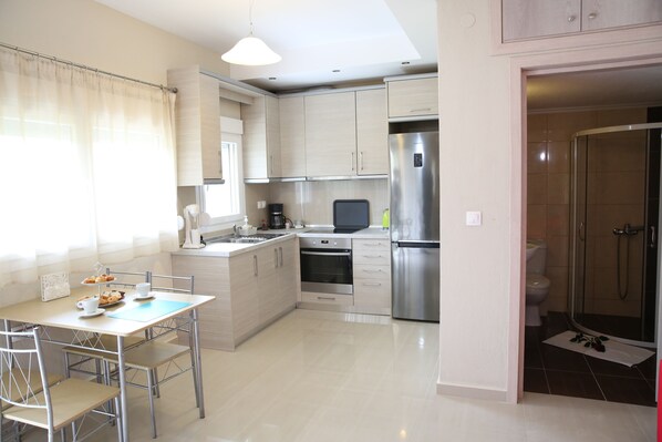 A modern kitchen with a dining area, stainless steel appliances, and a walk-in shower. - Villa Orama (Nea Propontida)