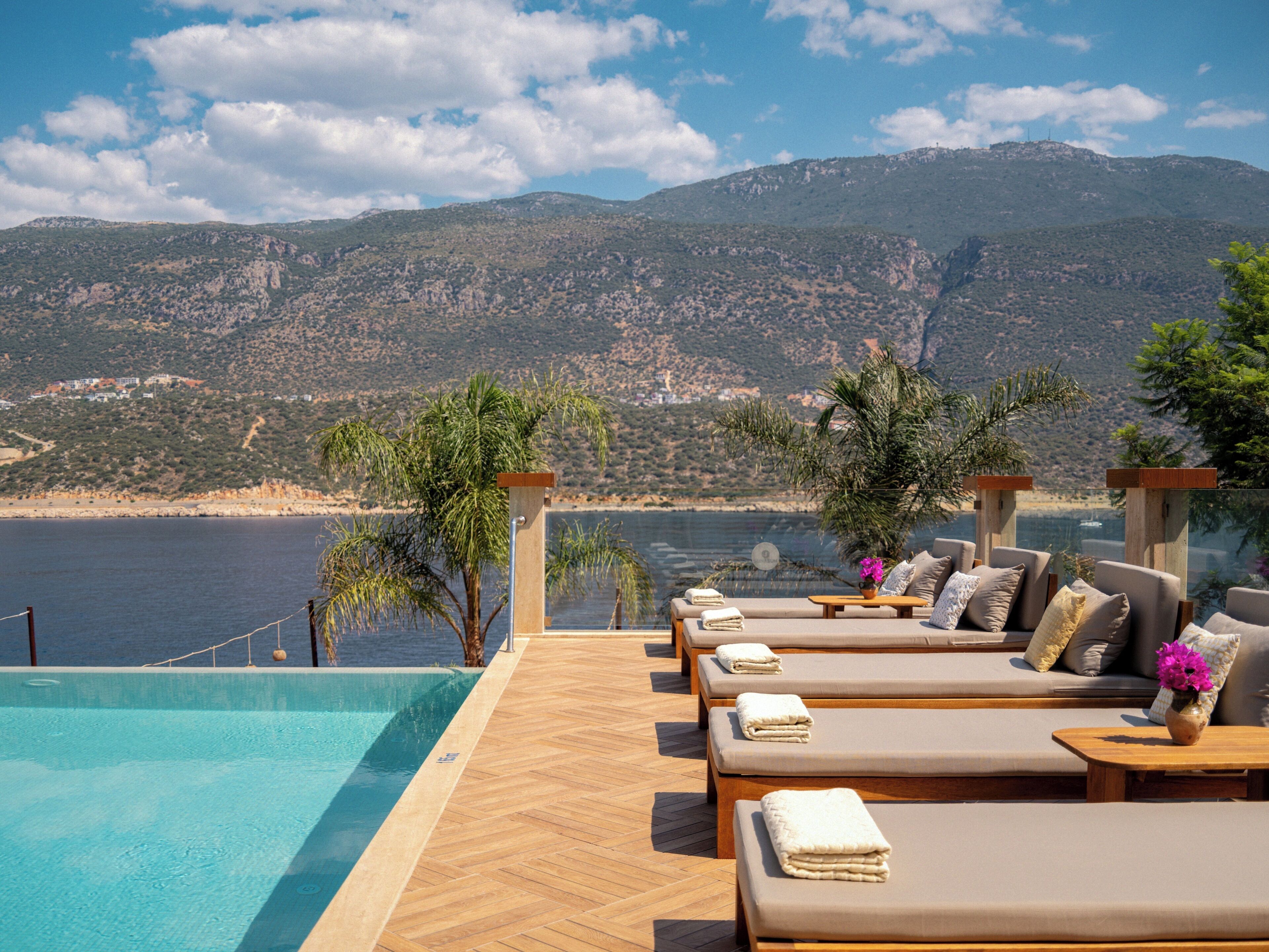 Zona junto a la piscina con sillones de descanso y vistas a un paisaje montañoso.