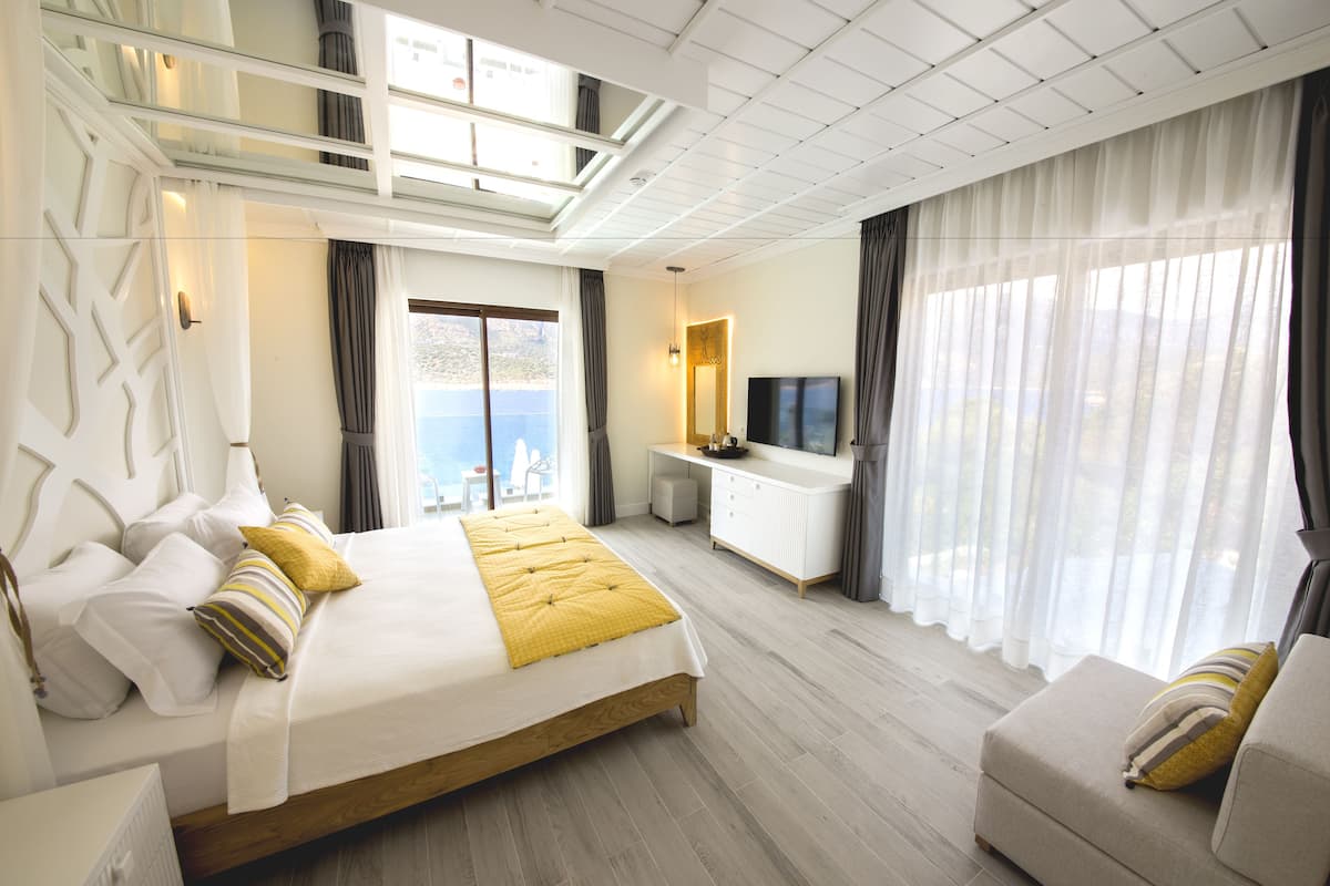 A modern hotel room with a large bed, a sofa, a TV, and a balcony with a city view.