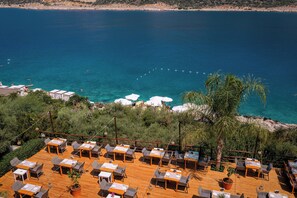Zona pranzo all'aperto con tavoli e sedie, con vista su un mare blu limpido.