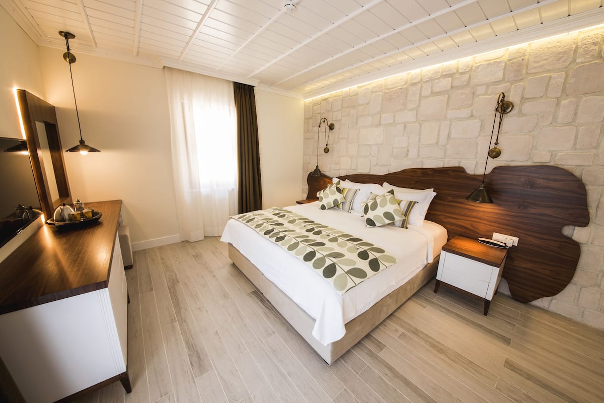 A modern bedroom with a wooden headboard, a bedside table, and a large bed with a leaf-patterned bedspread.