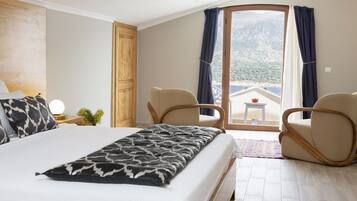 A hotel room with a large bed, two chairs, a small table, and a view of the mountains through a glass door.