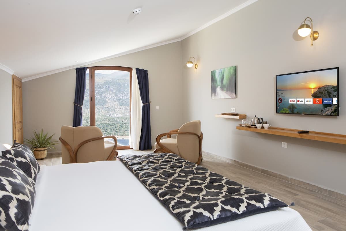 A hotel room with a bed, two chairs, a TV, a shelf with items, and a window with curtains.