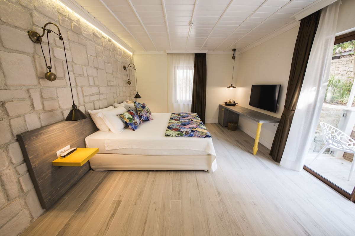 A modern bedroom with a brick wall, a bed with colorful bedding, a mounted TV, and a small table with a lamp.
