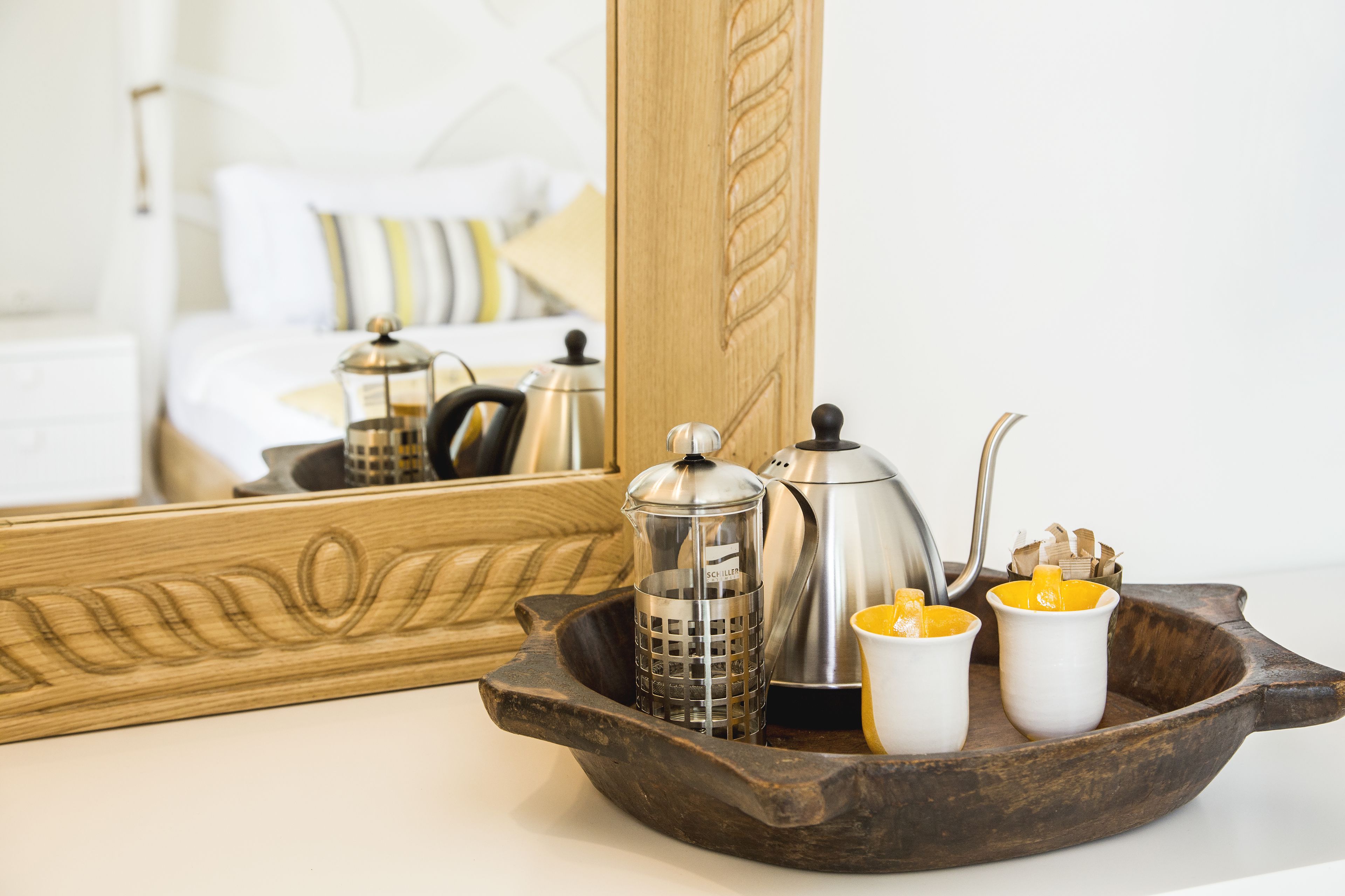 A wooden tray with a French press, a grinder, and two cups on a white countertop.