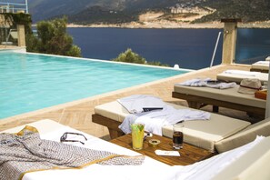 A poolside area with lounge chairs, a table with a drink, and a view of the sea. - Suna Sun Hotel (Kas)