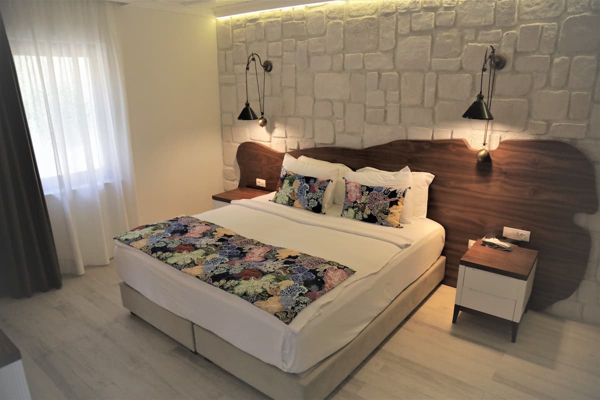 A modern bedroom with a large bed, two bedside tables, a nightstand, and a stone wall.