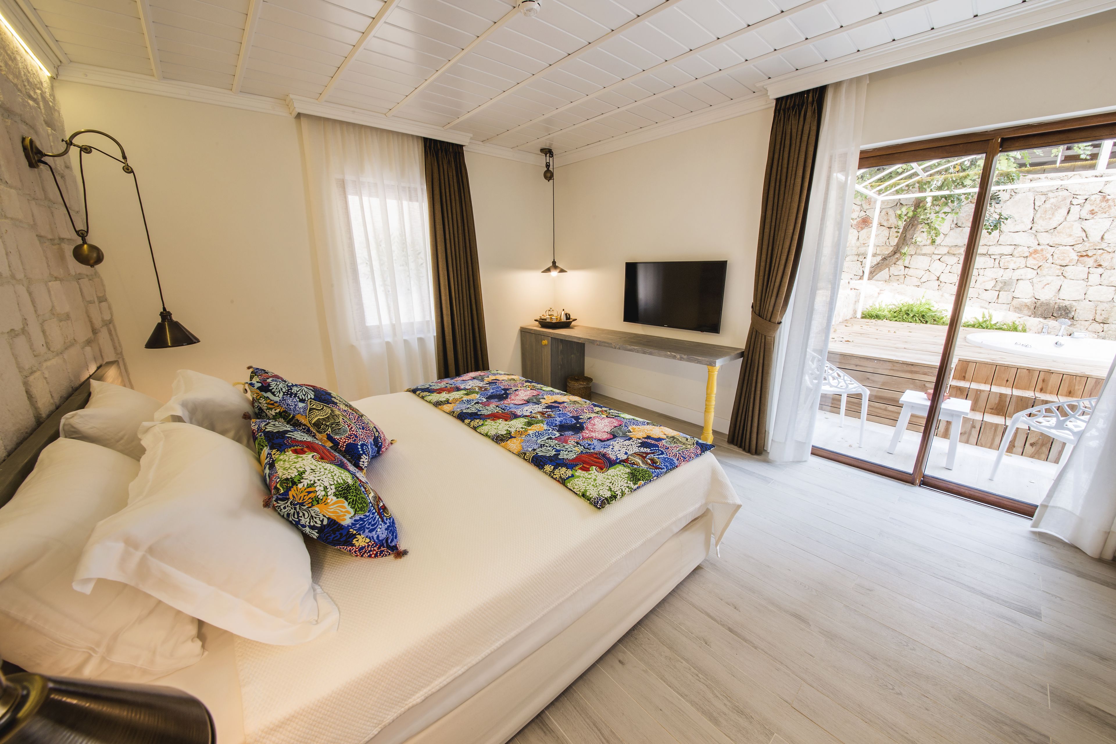 Een slaapkamer met een bed, een bureau met een televisie en uitzicht op een buitenruimte.