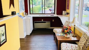A hotel room with a wooden floor, a desk with a lamp, a chair with a floral pattern, a window with a view of the outside, and a wall-mounted air conditioner. - Hampton Inn (not a Hilton Affiliate) Camp Hill - Harrisburg SW (Camp Hill)