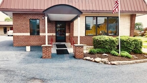 A brick building with a covered entrance, a flag, and a small garden area. - Hampton Inn (not a Hilton Affiliate) Camp Hill - Harrisburg SW (Camp Hill)