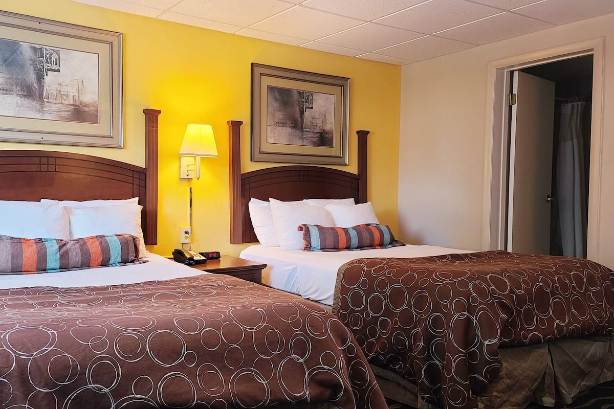 A hotel room with two beds, each with a patterned bedspread, a nightstand with a lamp, and framed artwork on the walls.