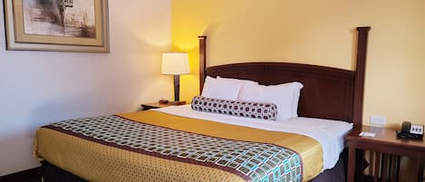 A hotel room with a large bed, a bedside table with a lamp, a framed picture on the wall, and a telephone on the nightstand.