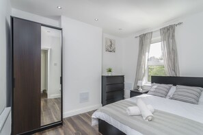 Un dormitorio con una cama grande, un armario de madera oscura, una mesita de noche con lámpara y un ventanal con cortinas.