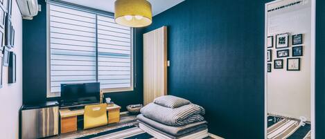 Una habitación pequeña con cama, escritorio, televisión y espejo.