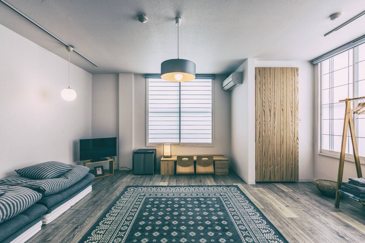 Una sala de estar moderna con un sofá, un televisor, un escritorio de madera, un tapete estampado y un ventanal con persianas.