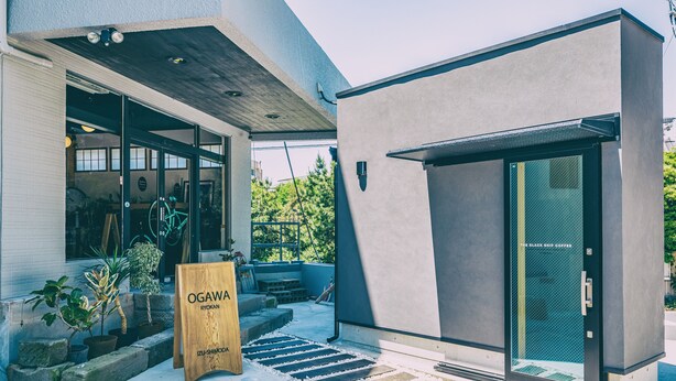 Un edificio moderno con puerta de cristal, un letrero de madera y plantas en macetas en el exterior.