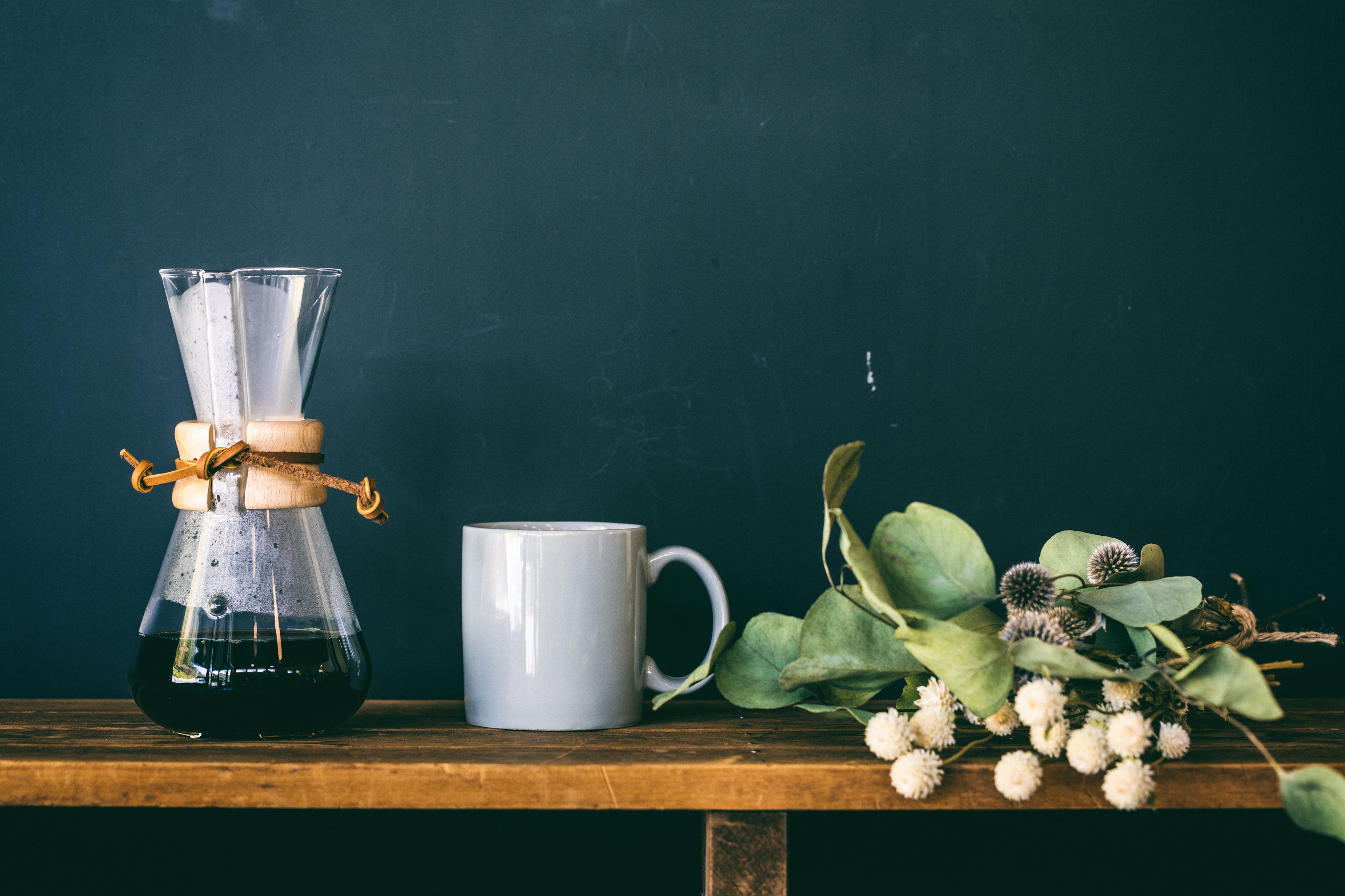 Una cafetera, una taza y algunas plantas sobre una superficie de madera.