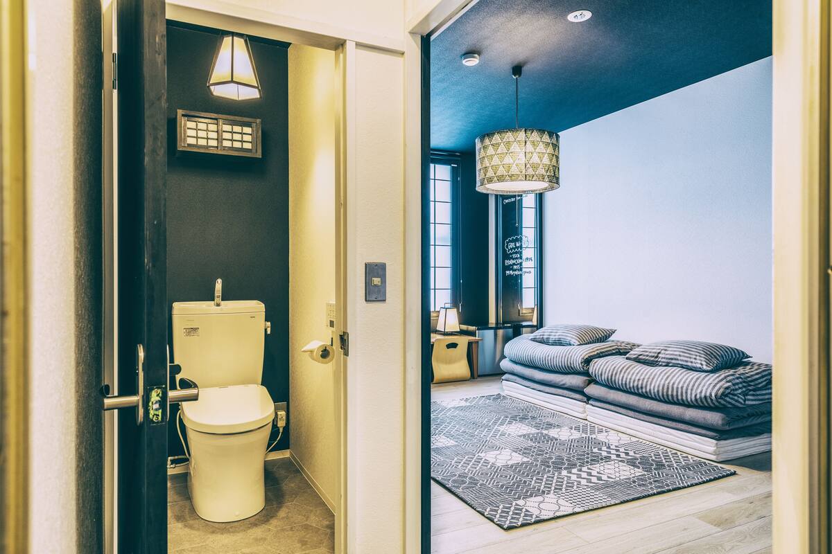 Un baño moderno con inodoro, una ventana pequeña y una lámpara fijada a la pared.
