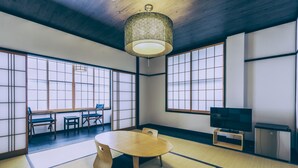 Una habitación al estilo japonés tradicional con suelo de tatami, una mesa baja, sillas, un televisor y una lámpara colgante decorativa.