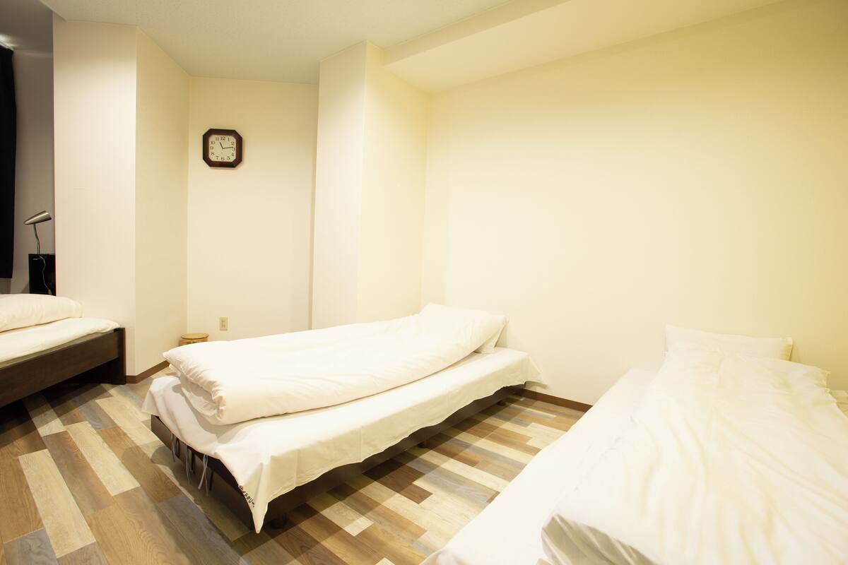 A room with two single beds, a wooden floor, a wall clock, and a small table.