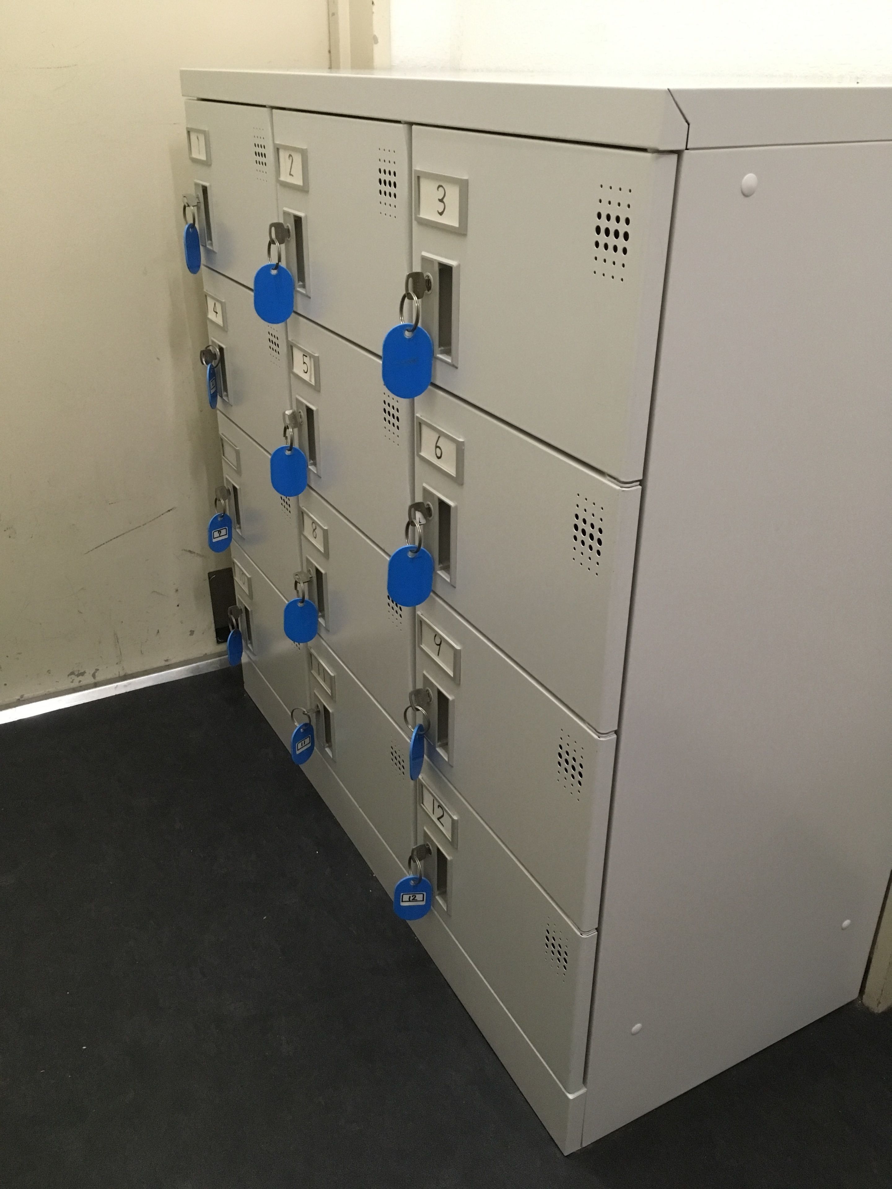 A row of grey lockers with blue tags, each labeled with a number from 1 to 12.