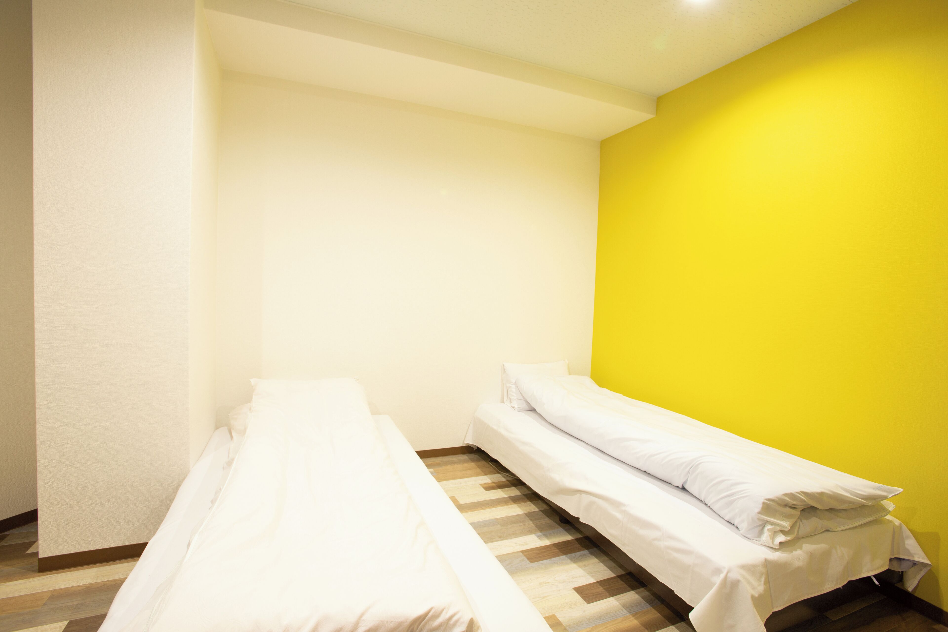A small, single-bed room with a wooden floor and a yellow accent wall.