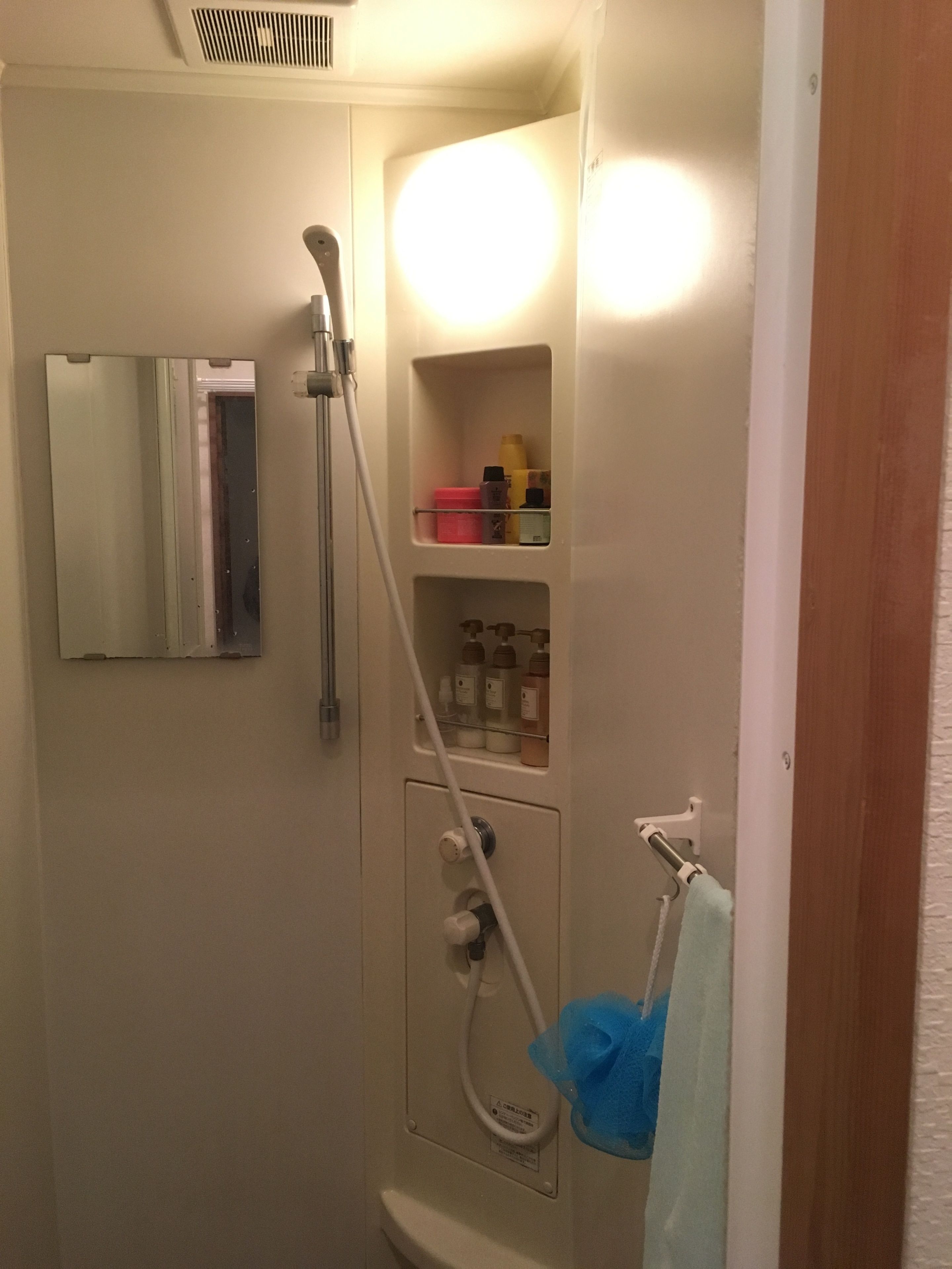 A bathroom with a shower, a mirror, and a shelf with toiletries.