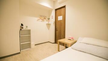 A bedroom with a bed, a small table, a wooden door, and a shelf with a hanging plant.