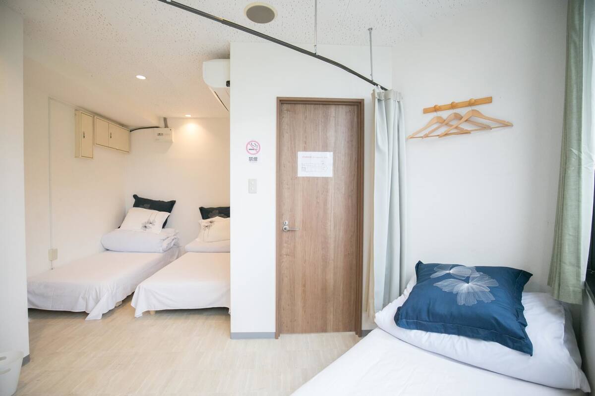 A small, clean room with two single beds, a wooden door, and a window with curtains.
