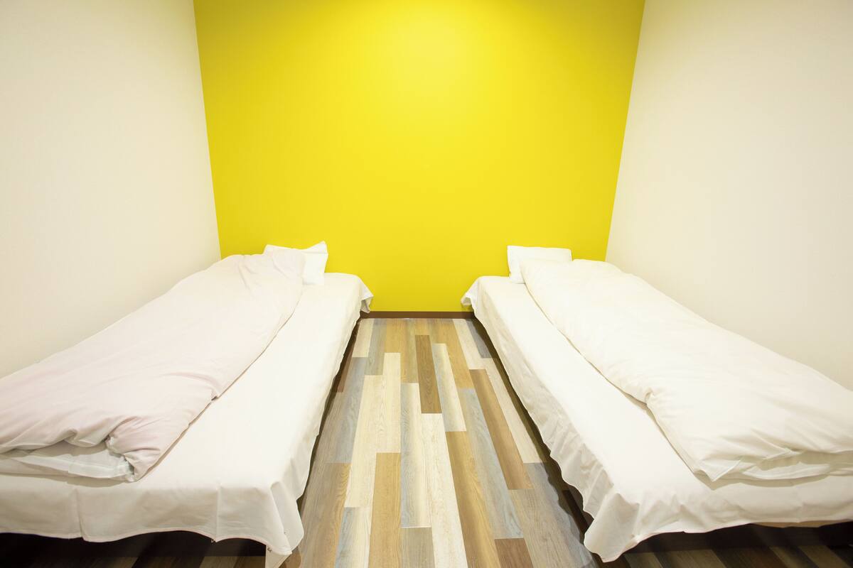 A room with two single beds, a wooden floor, and a yellow wall.