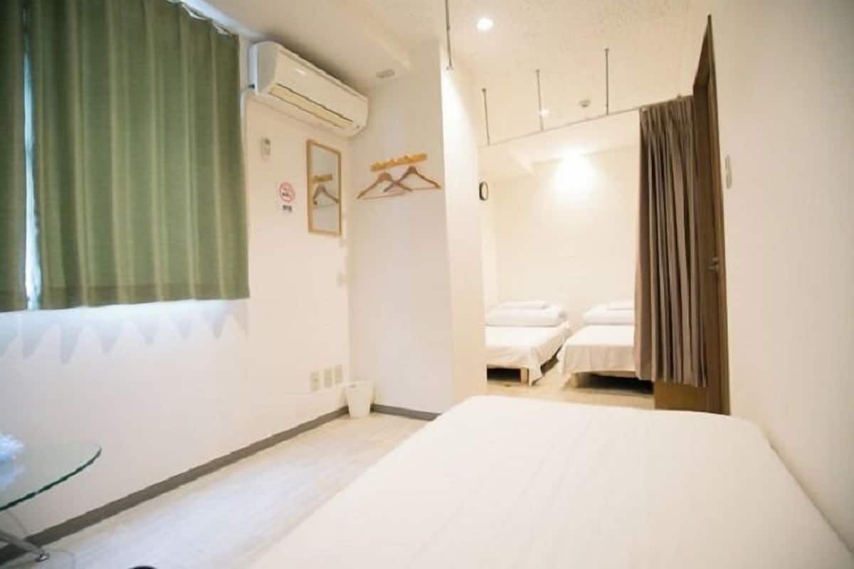 A hotel room with a large bed, a small bedside table, a hanging coat rack, and a window with curtains.