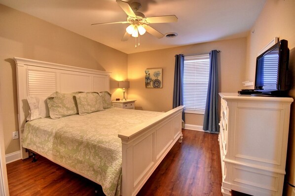 A bedroom with a bed, nightstand, lamp, ceiling fan, window with blinds, and a TV on a cabinet. - Tropical Paradise!! New Summer Discounts!!! (North Myrtle Beach)