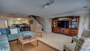 Una sala de estar con un sofá, una mesa de centro, un mueble para televisor y un sillón estampado.