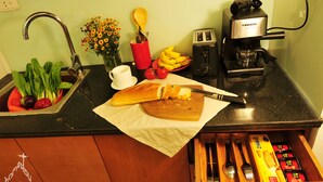 Una encimera de cocina con un tostador, una cafetera, una tabla de cortar con un cuchillo, un bol de fruta y un cajón con utensilios.