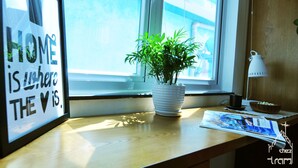 Una cita enmarcada sobre un alféizar, una planta en maceta, una lámpara y una revista sobre una mesa de madera.