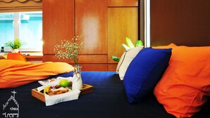 Una habitación con una cama, almohadones naranjas, una bandeja con comida, un florero con flores y una ventana que da a una piscina.