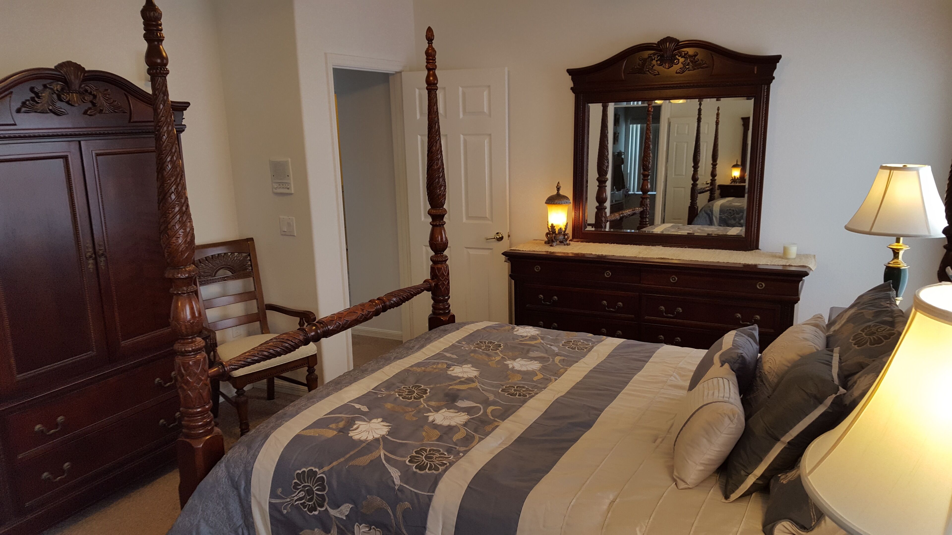 A bedroom with a four-poster bed, a dresser, a chair, and a mirror.