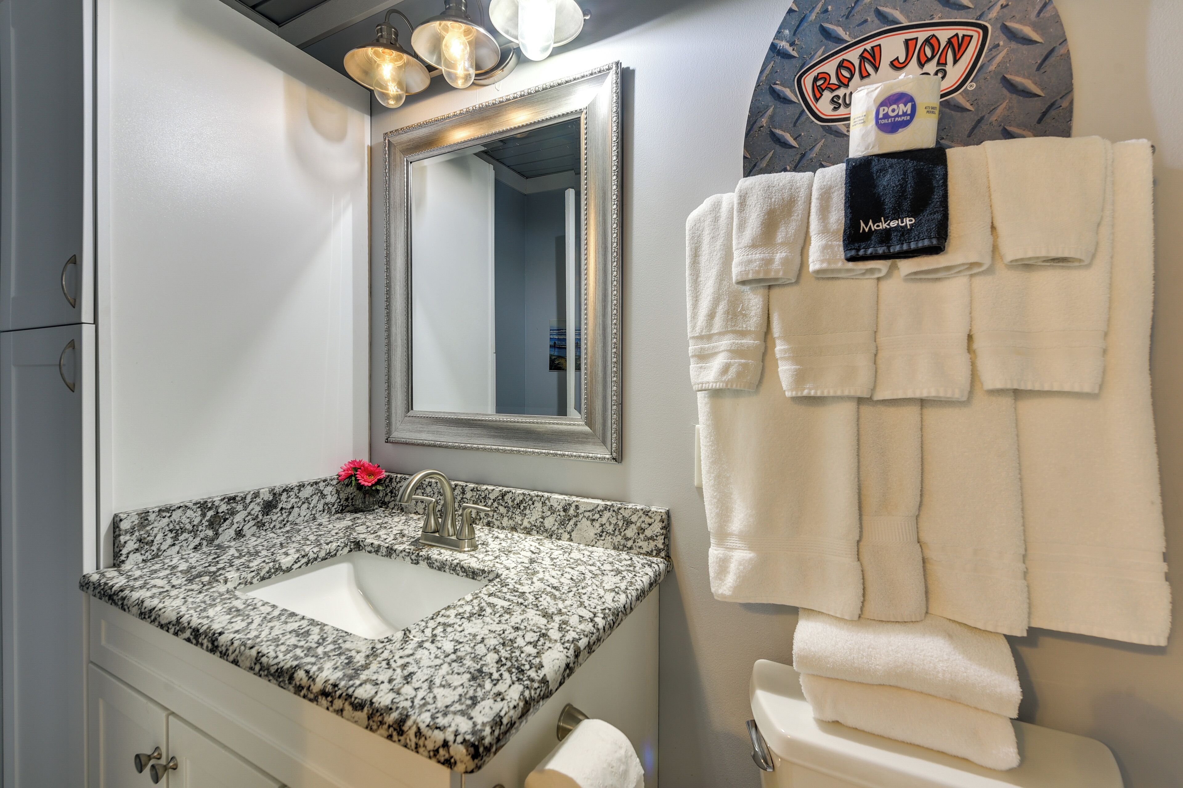 Un baño con lavamanos de granito, un espejo grande y un perchero con varias toallas.