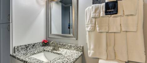 Un baño con lavamanos de granito, un espejo grande y un perchero con varias toallas.
