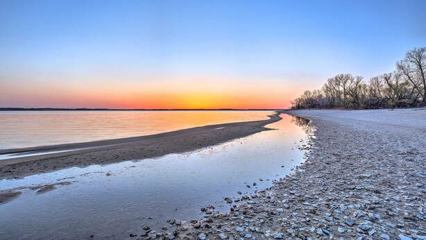 Een strand met stilstaand water dat de lucht weerspiegelt tijdens zonsondergang.
