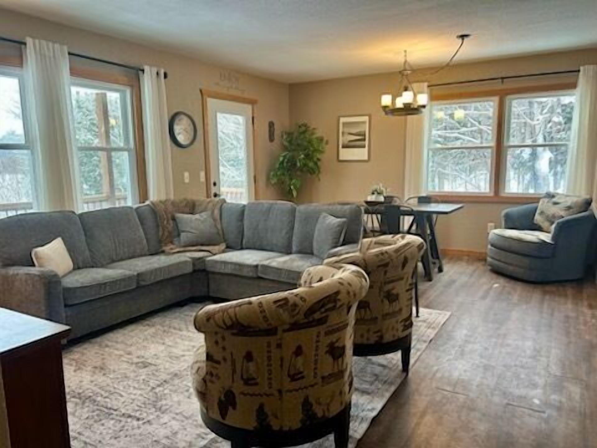 A living room with a sectional sofa, two armchairs, a dining table, and a chandelier.