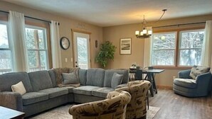 A living room with a sectional sofa, two armchairs, a dining table, and a chandelier.