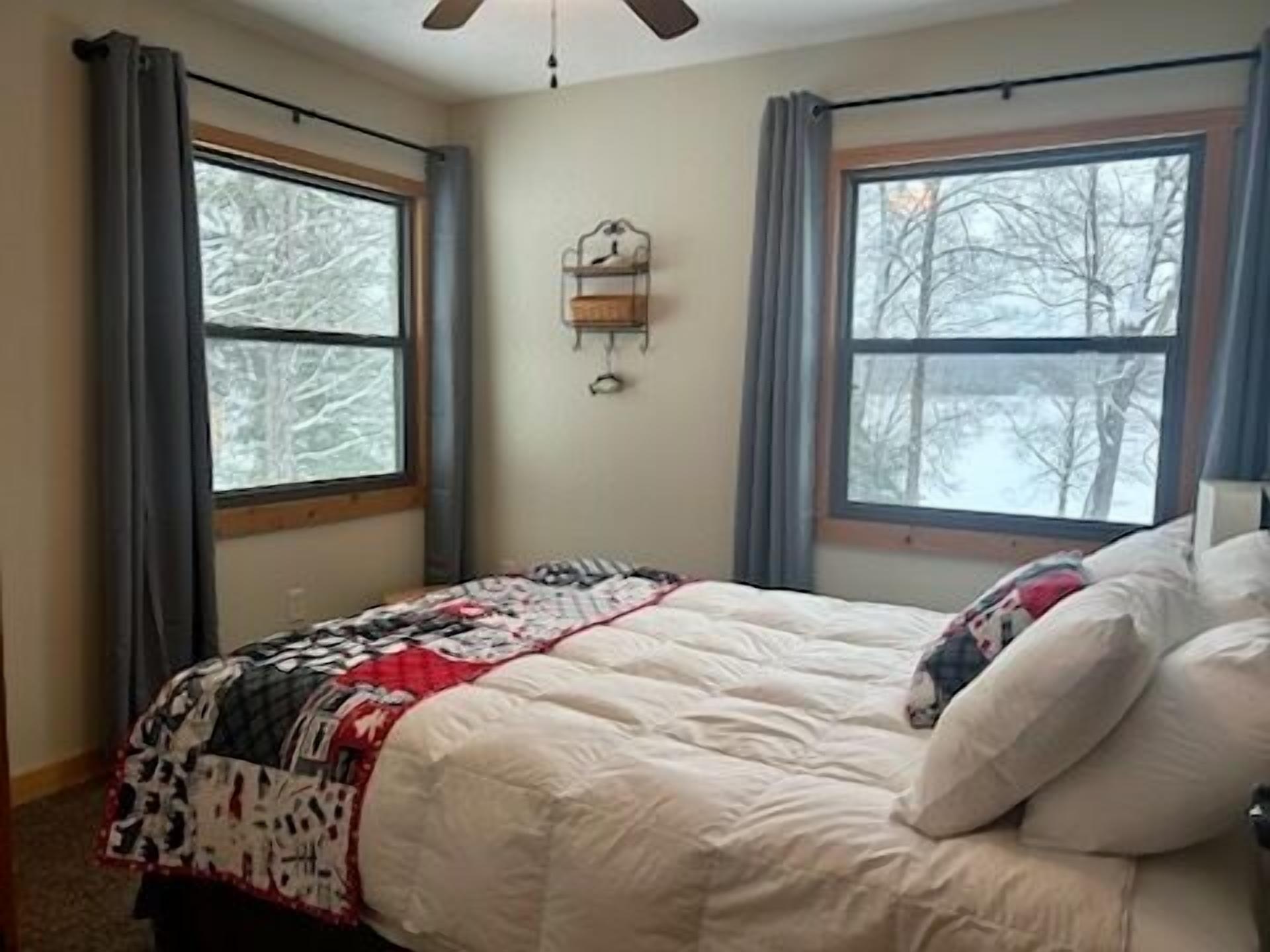 Une chambre à coucher avec un lit, deux fenêtres, une horloge murale et un ventilateur de plafond.