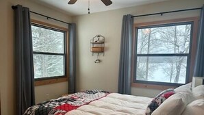 A bedroom with a bed, two windows, a wall clock, and a ceiling fan.