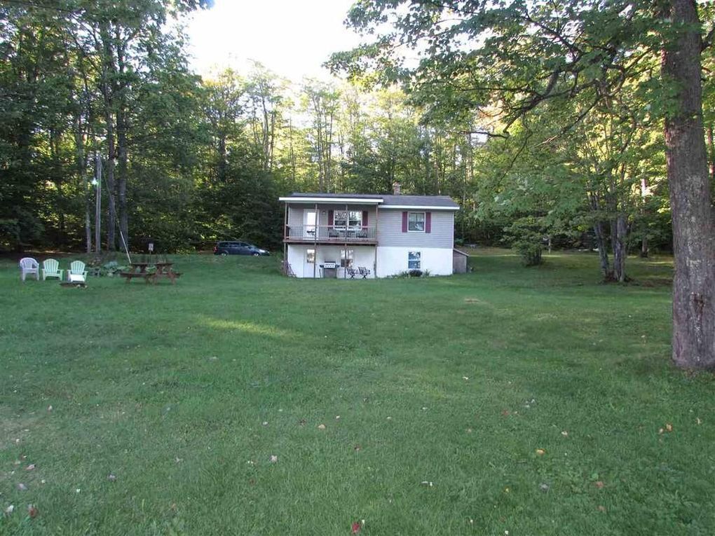 A two-story house with a balcony, surrounded by a grassy yard and trees.