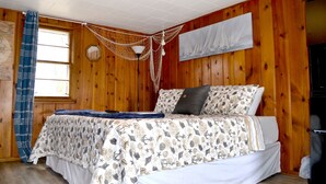 A wooden-paneled room with a bed, a hammock, and a large window.