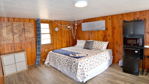 A cozy room with a bed, wooden walls, a window, a map, a microwave, and a refrigerator.