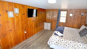 A wooden-paneled room with a bed, a television, and a window with curtains.