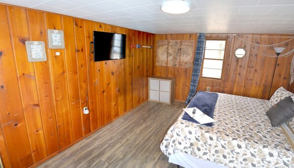 Una habitación con paneles de madera, una cama, un televisor y un ventanal con cortinas.